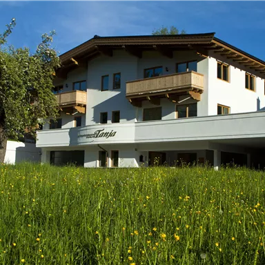 Ein gemütliches Haus mit Balkonen und einem schönen Garten. Die grünen Wiesen und der blaue Himmel verleihen der Umgebung eine einladende Atmosphäre.