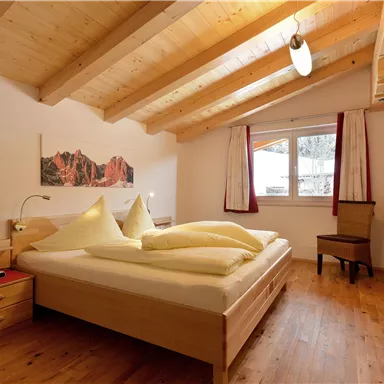 Ein helles Schlafzimmer mit Holzdecke und einem großen Bett. Neben dem Bett steht ein Nachttisch und ein Stuhl ist ebenfalls vorhanden.