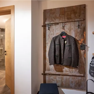 An elegant suit hangs on a rustic coat rack in a modern room. In the background, a bathroom with a shower is visible.