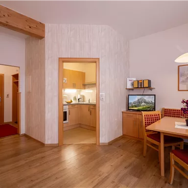 A cozy apartment with an open kitchen and a dining area. The space has a warm atmosphere with wooden flooring and friendly colors.