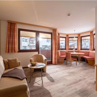 A cozy living space with a sofa, a table, and a seating area. Large windows provide plenty of daylight and a view of the outdoors.