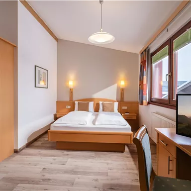 A simple and cozy hotel room with a double bed and a desk. Large windows provide plenty of daylight.