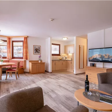 A cozy living room with modern furniture and a dining table. The open kitchen is well-equipped and the room is bright and welcoming.
