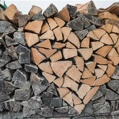 Ein Holzstapel mit einem Herz aus Holzteilen in der Mitte. Die Holzstücke sind ordentlich gestapelt und verleihen dem Bild eine warme Atmosphäre.