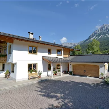 A beautiful house with a modern design and a balcony. In the background, mountains and a clear blue sky can be seen.