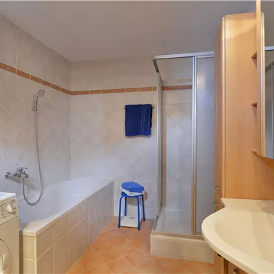 A modern bathroom with a bathtub and a shower. Blue towels are hanging on the wall, and a washing machine is in the corner.