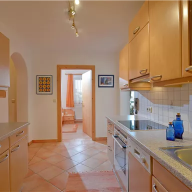 A bright kitchen with wooden cabinets and modern appliances. An adjacent room is visible in the background.