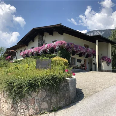 A beautiful house with colorful flowers and lots of green. The sky is clear and the surroundings are calm and inviting.