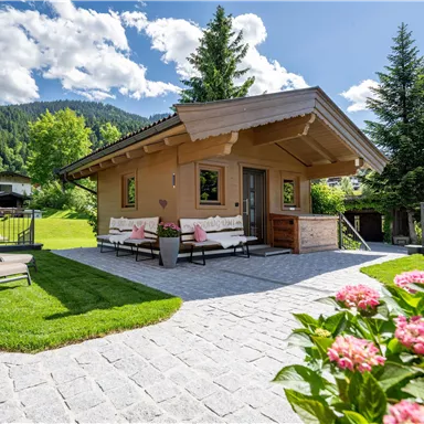 A cozy wooden house surrounded by green meadows and trees. The terrace invites relaxation, while blooming plants add a beautiful accent.