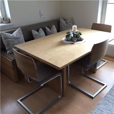 A stylish wooden dining table with modern chairs. In the background, there is a cozy bench with pillows and a decorative candle.