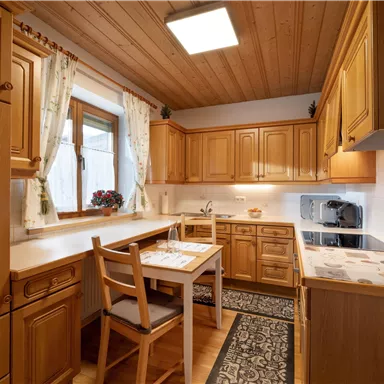 Eine gemütliche Küche mit Holzschränken und einem Esstisch. Die großen Fenster sorgen für helles Licht und eine angenehme Atmosphäre.