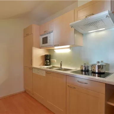 Eine moderne Küche mit hellen Holzschränken und einer eleganten Arbeitsfläche. Sie verfügt über grundlegende Küchengeräte und viel Stauraum.