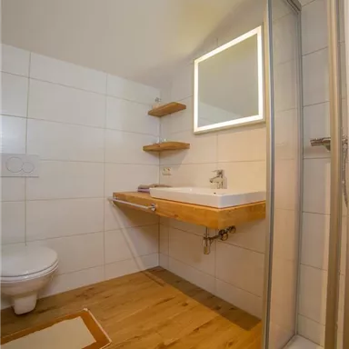 A modern bathroom with bright tiles and a wooden wash basin. The shower is separated by a glass wall.