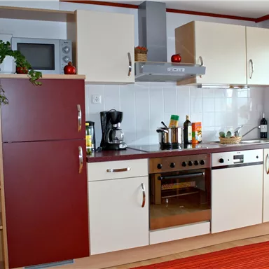 Moderne Küche mit weißen und roten Schränken. Es gibt einen Kühlschrank, einen Herd und eine Mikrowelle, sowie einige Pflanzen und Kochutensilien.