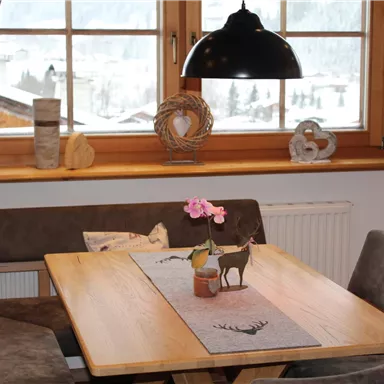 Ein gemütlicher Essbereich mit einem Holztisch und bequemen Stühlen. Durch die Fenster ist eine verschneite Landschaft zu sehen.