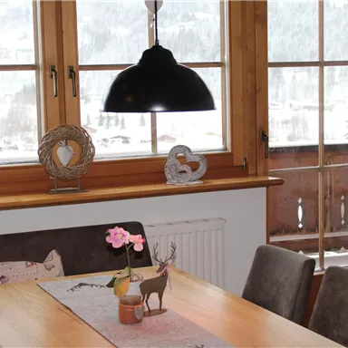 Ein gemütlicher Essbereich mit einem Holztisch und modernen Stühlen. Große Fenster bieten einen Blick auf eine verschneite Landschaft.