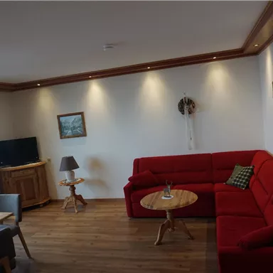 Ein gemütliches Wohnzimmer mit einem roten Sofa und einem Holztisch. Es gibt einen Fernseher und einige Bilder an der Wand.