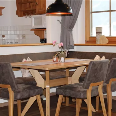 Ein gemütlicher Essbereich mit einem quadratischen Tisch und sechs Stühlen. Eine Bank sorgt für zusätzlichen Platz und eine warme Atmosphäre.