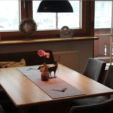 Ein gemütlicher Essbereich mit einem Holz-Tisch und modernen Stühlen. Auf dem Tisch steht eine Blume in einer Vase und eine kleine Figur eines Rehs.