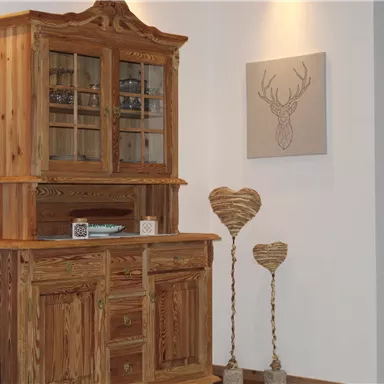 Ein rustikales Holzschrankensemble steht an der Wand. Darunter befinden sich dekorative Herzen und ein Bild einer Hirschsilhouette.