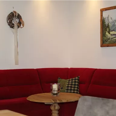 Ein gemütliches Wohnzimmer mit einem roten Sofa und einem Holztisch. An der Wand hängt ein Gemälde von Bergen und einem Fluss.