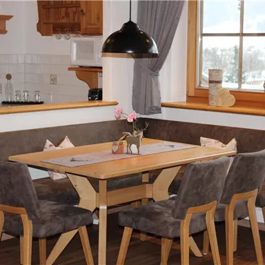 Ein gemütlicher Essbereich mit einem Holztisch und gepolsterten Stühlen. Große Fenster sorgen für viel Licht und einen Blick auf die winterliche Landschaft.