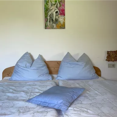 Ein gemütliches Schlafzimmer mit einem großen Bett und blauen Kissen. An der Wand hängt ein buntes Bild eines Pferdes.