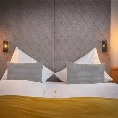 Ein gemütliches Schlafzimmer mit einem großen Bett und dekorativen Kissen. Sanfte Beleuchtung und elegante Wände schaffen eine entspannende Atmosphäre.