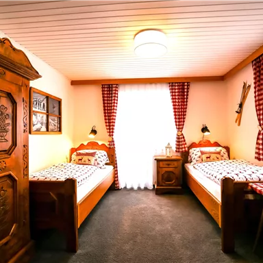 Ein gemütliches Schlafzimmer mit zwei Einzelbetten und rustikalen Holzmöbeln. Helle Farben und einladende Fenster mit karierten Vorhängen schaffen eine warme Atmosphäre.