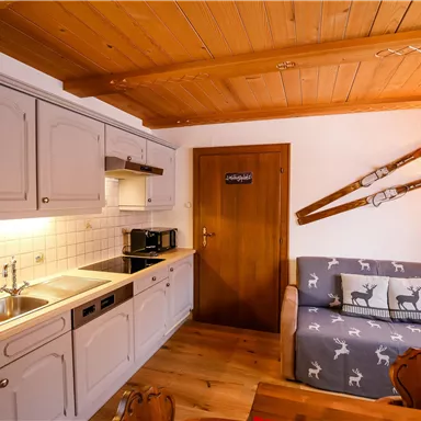 Eine gemütliche Küche mit modernen Geräten und einem Wohnbereich. An der Wand hängen Skier, und der Raum hat ein rustikales Holzdesign.