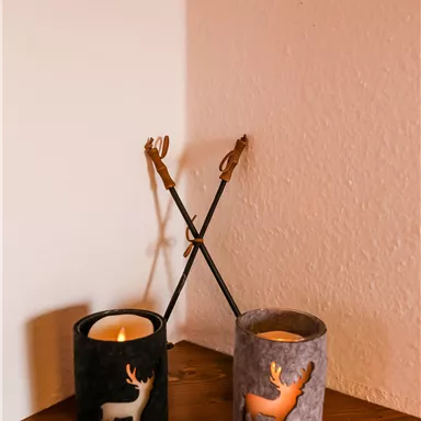 Zwei dekorative Kerzenhalter in Schwarz und Grau mit Rentier-Motiven stehen auf einem Tisch. Im Hintergrund sieht man eine helle Wand.