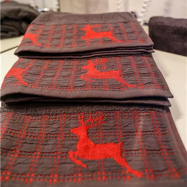 Gestapelte Handtücher in Grau mit roten Rentier-Motiven. Die handgefertigten Tücher haben ein dekoratives Karomuster.