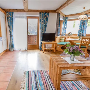 A cozy living space with wooden details and colorful curtains. The room is bright and inviting, with a small table and a television.