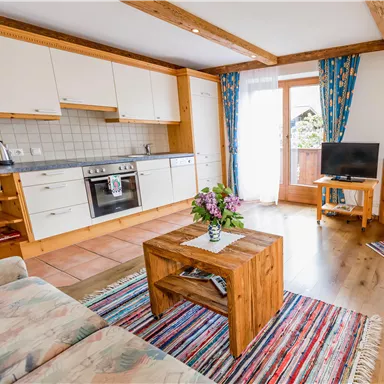 A cozy apartment with a modern kitchen and a living room. The space is bright and friendly, with a wooden coffee table and colorful curtains.