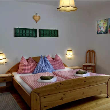 Ein gemütliches Schlafzimmer mit einem Holzbett und bunten Kissen. Die Wände sind hell gestrichen und es gibt eine schöne Dekoration.