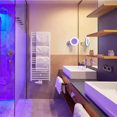 Ein modernes Badezimmer mit einer Dusche und eleganten Waschbecken. Sanfte, bunte Beleuchtung schafft eine entspannte Atmosphäre.