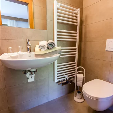 Ein modernes Badezimmer mit fliesenverkleideten Wänden. Es verfügt über ein Waschbecken, eine Toilette und Handtücher.