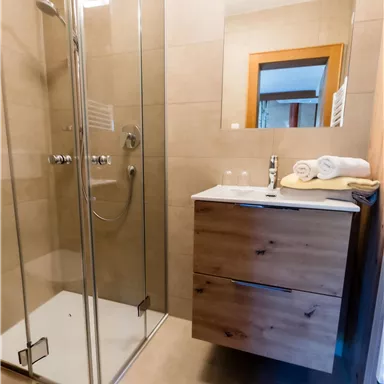 Ein modernes Badezimmer mit einer klaren Glasdusche und einem Holzwaschtisch. Frische Handtücher liegen bereit.