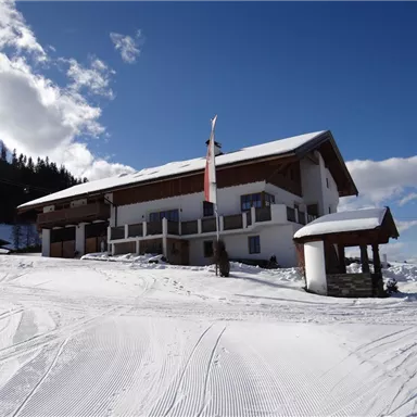 A charming mountain house in a snowy landscape. The sky is blue with a few clouds and the slope is well groomed.