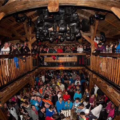 A bustling venue with many people on two floors. The wood-paneled surroundings and the dense gathering of guests create a lively atmosphere.