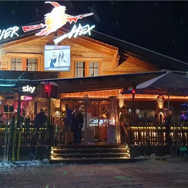 A cozy après-ski venue with wooden paneling and colorful lights. Many people are standing outside, enjoying the atmosphere.
