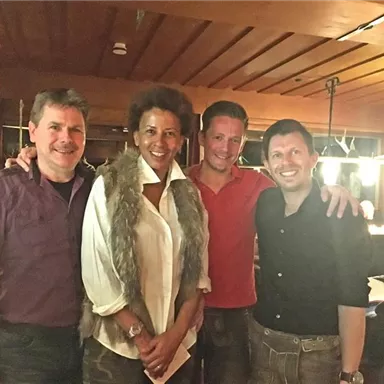 Vier Personen in einem gemütlichen Restaurant. Sie lächeln und posieren für das Foto vor einer warmen, einladenden Atmosphäre.