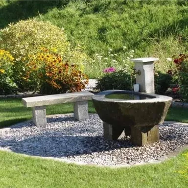 A beautiful garden with a stone table and a water fountain.  
Surrounded by colorful flowers and green grass.