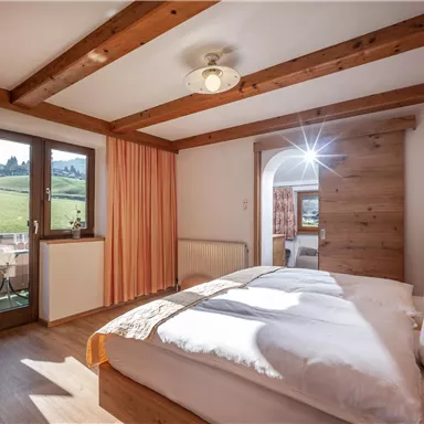 Ein gemütliches Schlafzimmer mit einem großen Bett und Holzdekor. Große Fenster mit Blick auf die Landschaft sorgen für viel Tageslicht.
