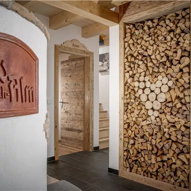 An inviting hallway with a rustic wood stack and a stylish sign. The walls are painted in neutral tones, and the wooden elements create a cozy atmosphere.