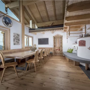 A cozy interior with wooden furniture and a large dining table. In the background are windows overlooking the mountains and a fireplace that creates a warm atmosphere.