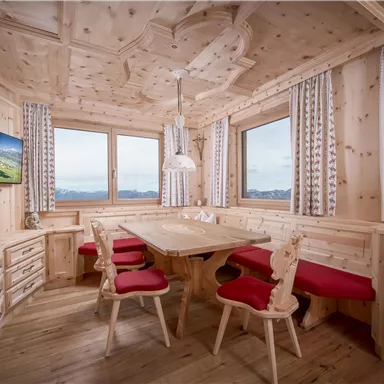 A cozy wooden kitchen with a large table and red chairs. The windows offer a beautiful view of the mountains.