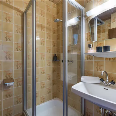 A small bathroom with a shower and a sink. The walls are decorated with a light tile design.