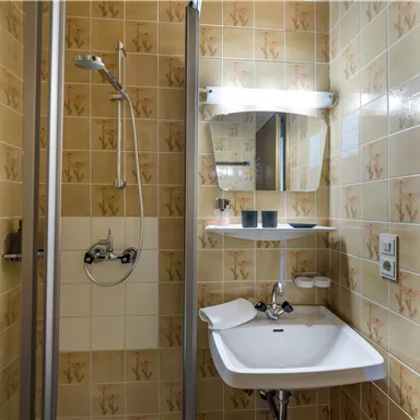 A small bathroom with a shower and sink. The walls are decorated with a beige tile pattern.