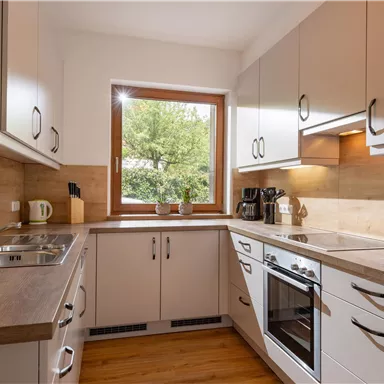 A modern kitchen with white cabinets and wooden elements. The room has a large window that lets in plenty of natural light.